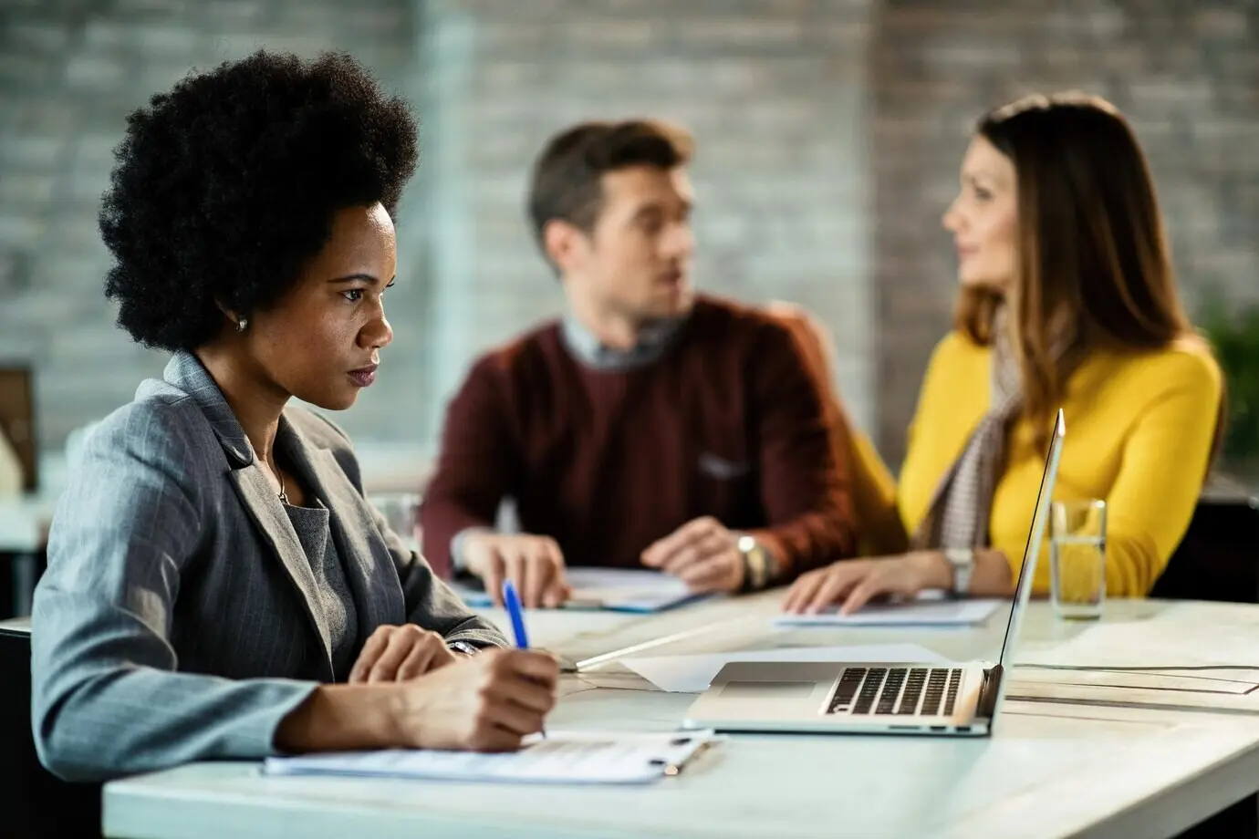 Eine schwarze Bankmanagerin nutzt einen Laptop und schreibt Notizen, während sie im Büro eine Besprechung mit einem Paar hat.